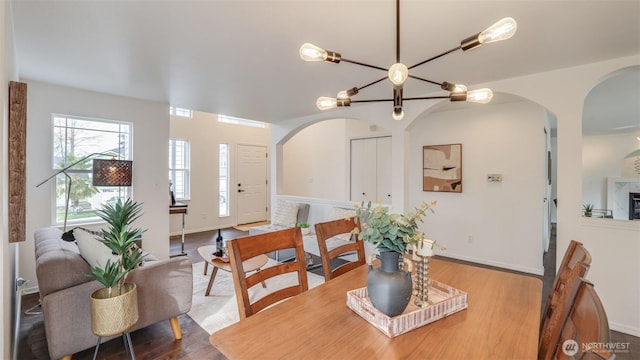 dining space featuring arched walkways, a notable chandelier, baseboards, and wood finished floors