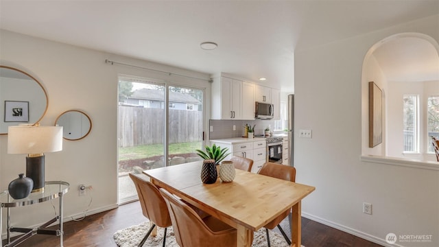 dining space featuring baseboards, arched walkways, dark wood-type flooring, and a healthy amount of sunlight