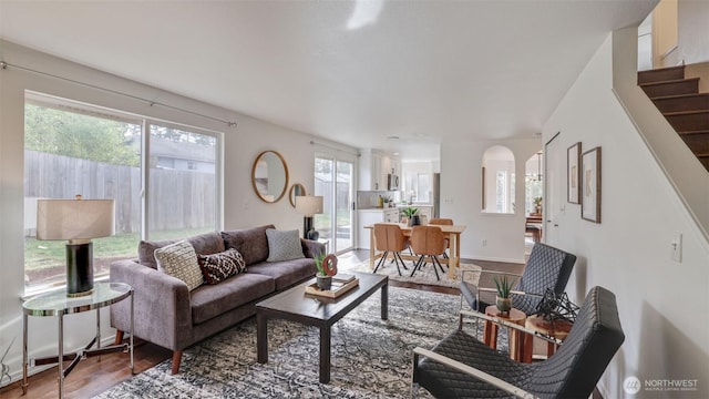 living room with stairs, wood finished floors, arched walkways, and baseboards