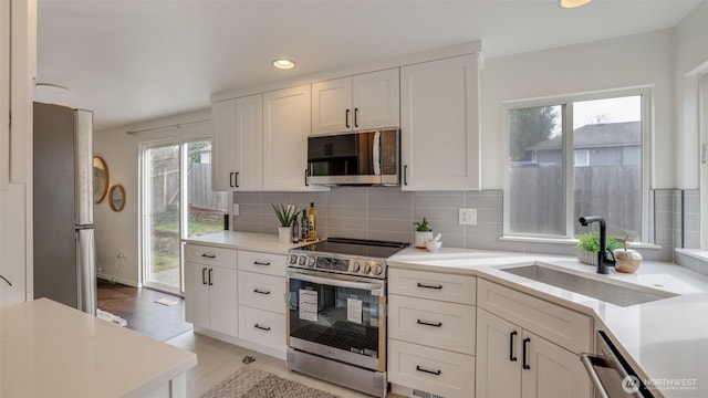 kitchen with tasteful backsplash, white cabinetry, stainless steel appliances, and a sink