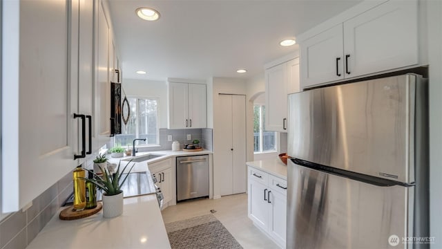 kitchen with decorative backsplash, appliances with stainless steel finishes, arched walkways, white cabinetry, and a sink