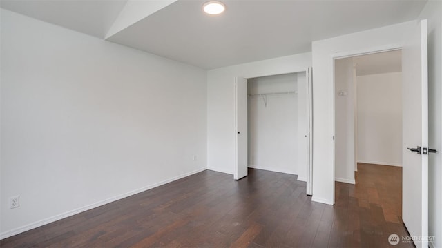 unfurnished bedroom with a closet, dark wood-type flooring, and baseboards