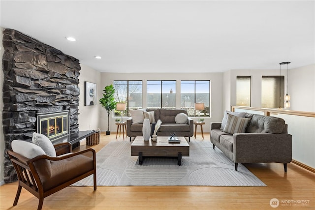 living room featuring recessed lighting, baseboards, a stone fireplace, and wood finished floors