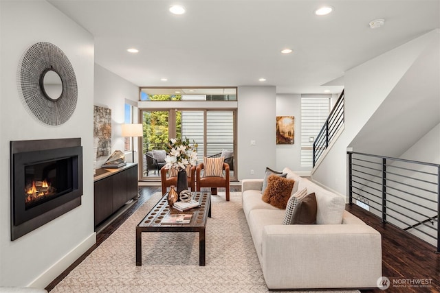 living area featuring stairway, wood finished floors, baseboards, recessed lighting, and a glass covered fireplace