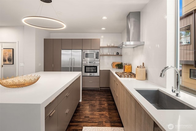 kitchen featuring built in appliances, gray cabinetry, wall chimney range hood, and a sink