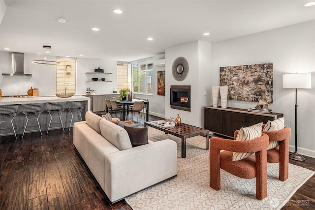 living room with hardwood / wood-style floors, baseboards, recessed lighting, a warm lit fireplace, and an AC wall unit