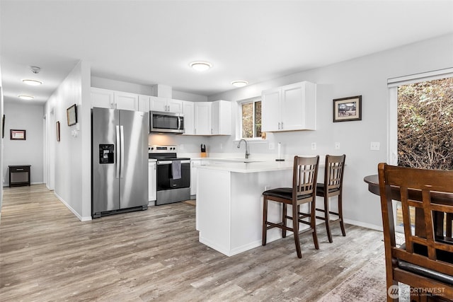 kitchen featuring a peninsula, light countertops, light wood-style floors, and appliances with stainless steel finishes