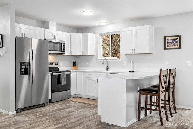 kitchen featuring a kitchen bar, appliances with stainless steel finishes, a peninsula, light wood-style floors, and a sink