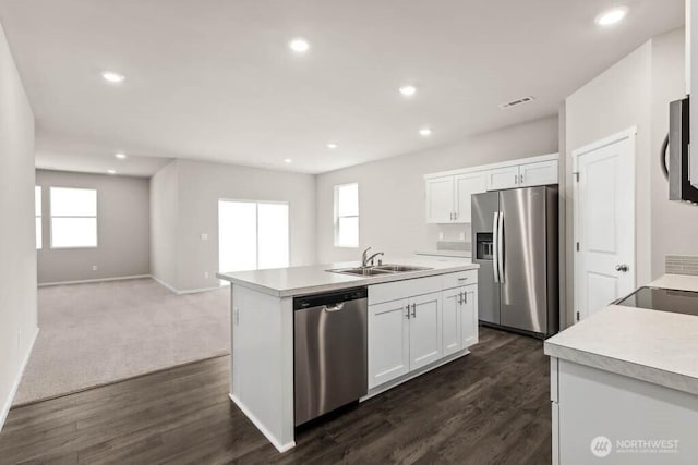 kitchen with a sink, stainless steel appliances, a kitchen island with sink, and white cabinets