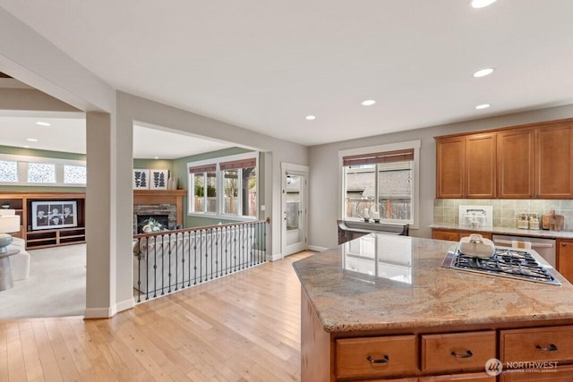 kitchen featuring light stone counters, decorative backsplash, a stone fireplace, and a wealth of natural light