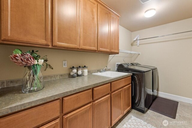 clothes washing area featuring washer and clothes dryer, a sink, cabinet space, light tile patterned flooring, and baseboards