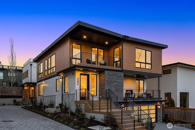 contemporary home with a balcony, fence, and stone siding