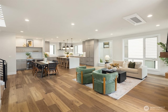 living area featuring recessed lighting, light wood-style flooring, beverage cooler, and stairway