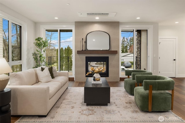 living area featuring a multi sided fireplace, visible vents, recessed lighting, and wood finished floors