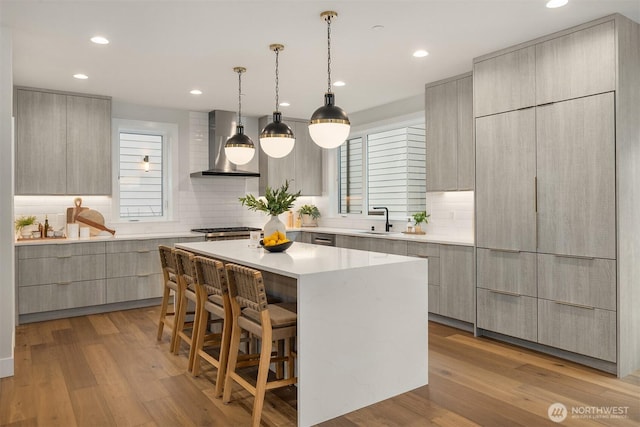 kitchen featuring a center island, wall chimney exhaust hood, modern cabinets, and a sink