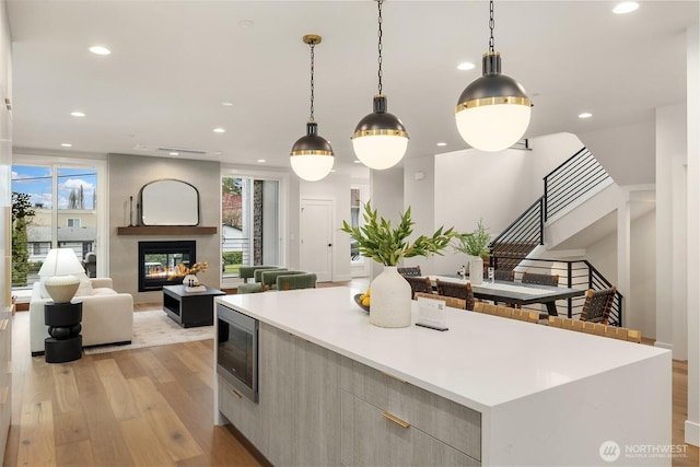 kitchen with a glass covered fireplace, stainless steel microwave, modern cabinets, light wood-type flooring, and a wealth of natural light