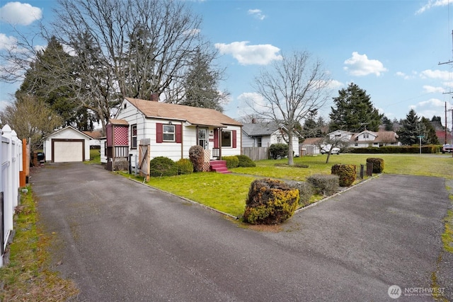 view of front of property with a detached garage, a front lawn, fence, aphalt driveway, and an outbuilding