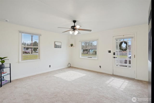 carpeted empty room featuring a healthy amount of sunlight, a ceiling fan, and baseboards