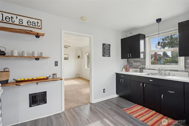 kitchen with a sink, backsplash, dark cabinetry, and light countertops