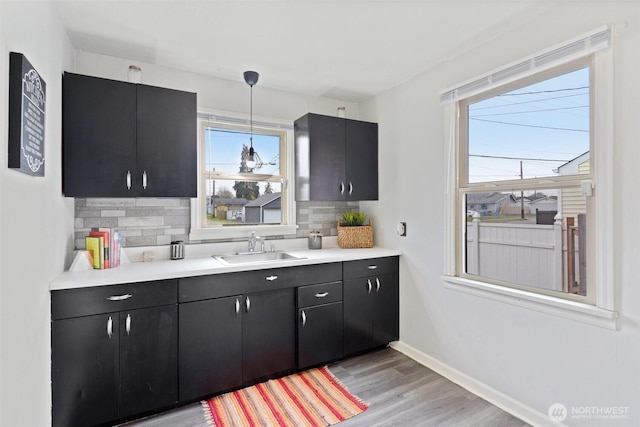 kitchen with dark cabinetry, baseboards, a sink, decorative backsplash, and light countertops