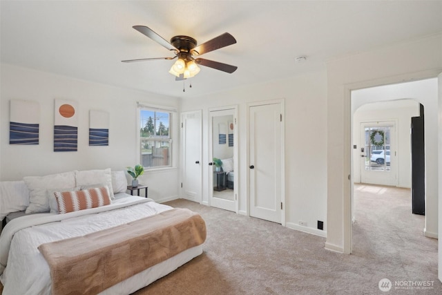 carpeted bedroom featuring arched walkways, ceiling fan, baseboards, and multiple closets