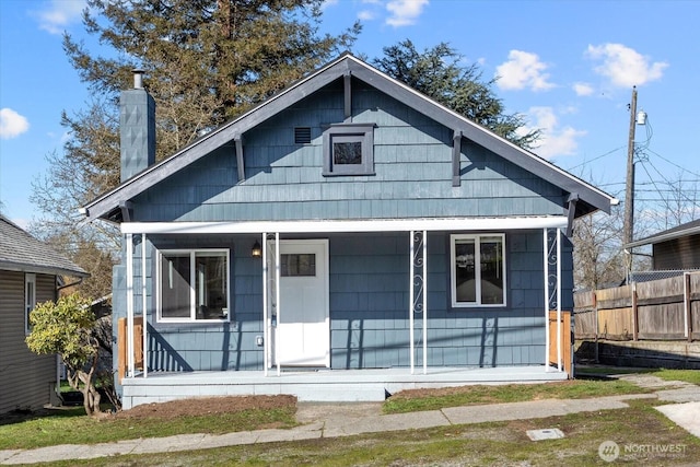 bungalow-style home featuring covered porch, a chimney, and fence