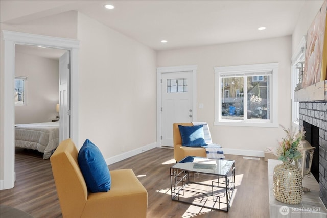 living area with recessed lighting, baseboards, a brick fireplace, and wood finished floors