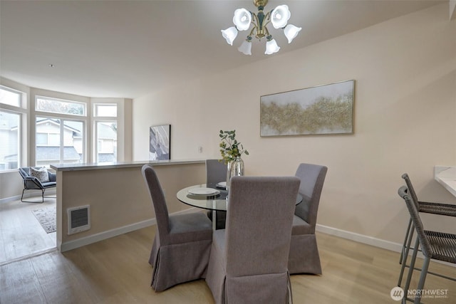 dining area with light wood-style flooring, a notable chandelier, baseboards, and visible vents