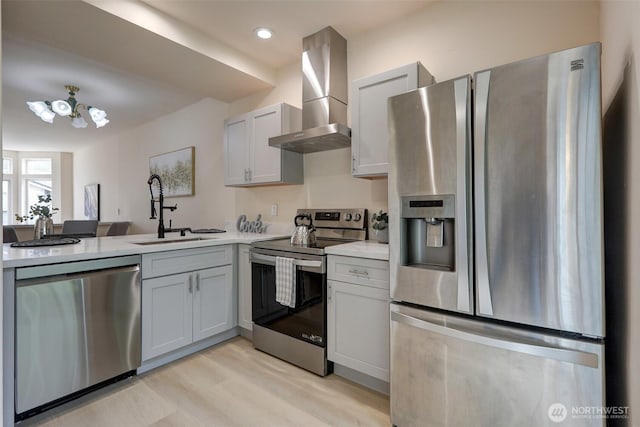 kitchen with light wood finished floors, a sink, light countertops, appliances with stainless steel finishes, and wall chimney exhaust hood