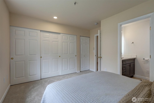 bedroom featuring baseboards, ensuite bath, recessed lighting, multiple closets, and light carpet