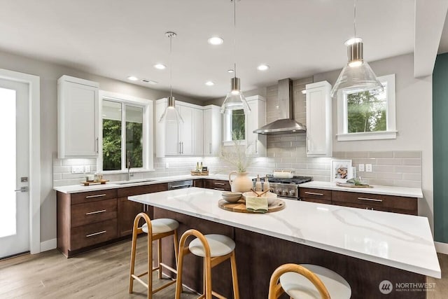 kitchen with a kitchen bar, a sink, wall chimney exhaust hood, white cabinets, and stove