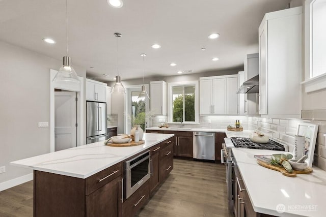 kitchen featuring dark wood-type flooring, wall chimney range hood, high quality appliances, backsplash, and a center island