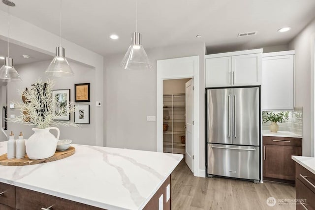 kitchen with light wood-type flooring, visible vents, pendant lighting, high end fridge, and light stone countertops