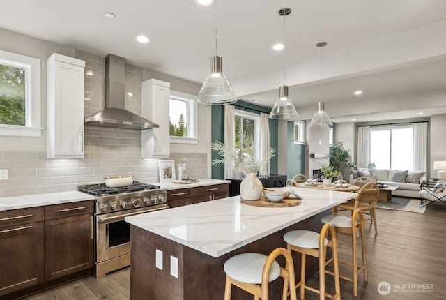 kitchen featuring tasteful backsplash, high end stainless steel range, open floor plan, wood finished floors, and wall chimney exhaust hood