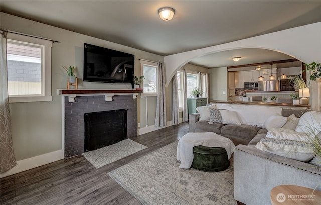 living area featuring baseboards, arched walkways, wood finished floors, and a fireplace