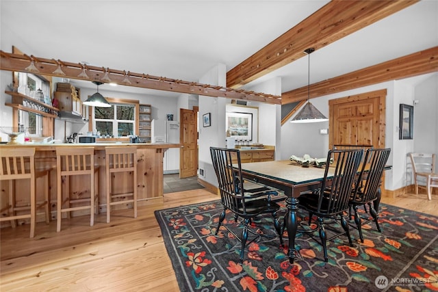 dining space featuring light wood finished floors, beam ceiling, and visible vents