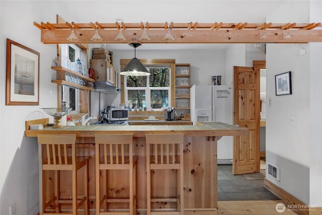 kitchen with visible vents, tile counters, a kitchen breakfast bar, a peninsula, and open shelves