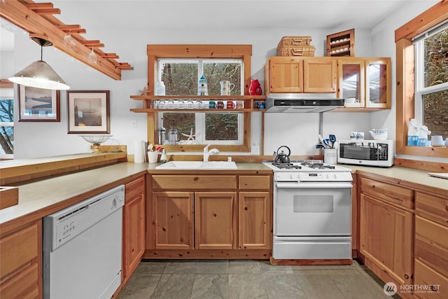 kitchen featuring white appliances, a sink, light countertops, decorative light fixtures, and exhaust hood