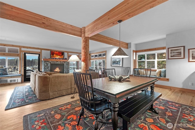 dining space featuring beamed ceiling, wood finished floors, baseboards, and a warm lit fireplace