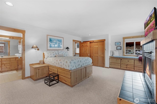 bedroom featuring light carpet, baseboards, ensuite bath, and a closet