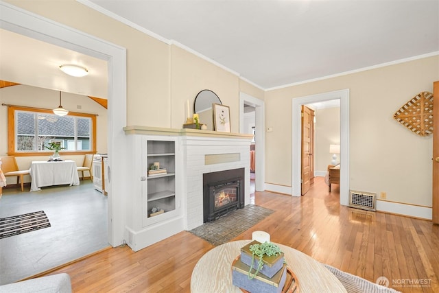 living room with hardwood / wood-style flooring, a fireplace with flush hearth, visible vents, and ornamental molding