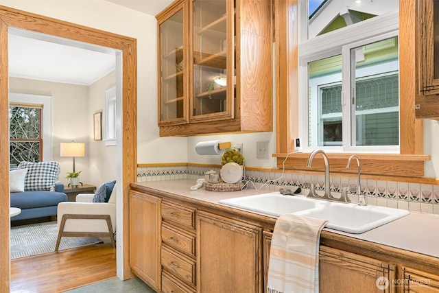 kitchen featuring brown cabinets, ornamental molding, a sink, light countertops, and glass insert cabinets