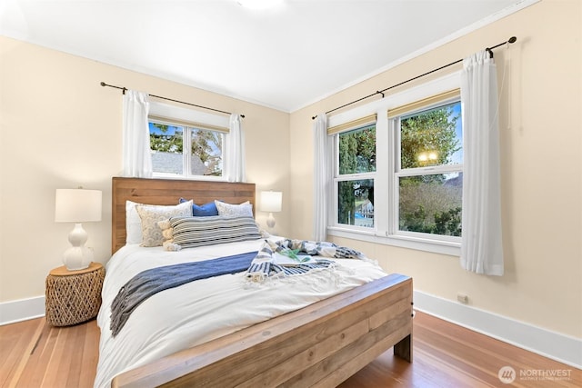 bedroom with multiple windows, crown molding, baseboards, and wood finished floors