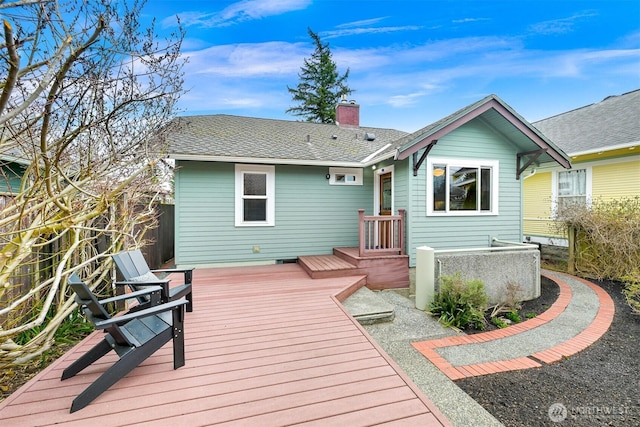 back of house with a wooden deck, a chimney, roof with shingles, and fence