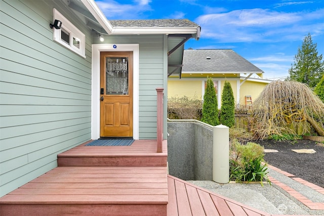 view of exterior entry with fence and a shingled roof