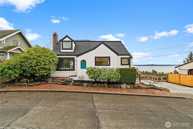 view of front facade featuring a water view, a shingled roof, a chimney, and fence