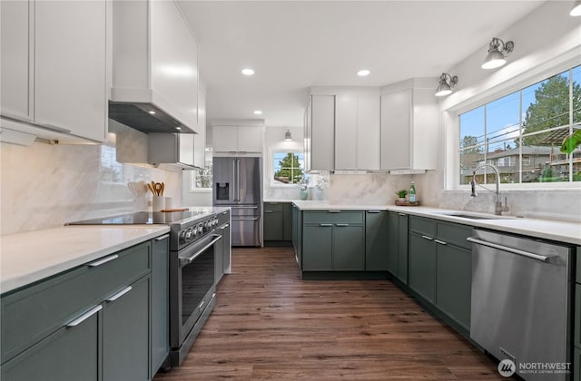 kitchen featuring a sink, light countertops, white cabinetry, wall chimney range hood, and premium appliances