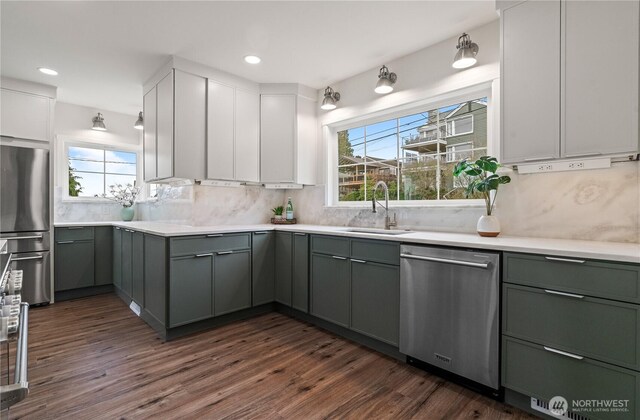 kitchen with a sink, backsplash, gray cabinetry, stainless steel appliances, and dark wood-style flooring