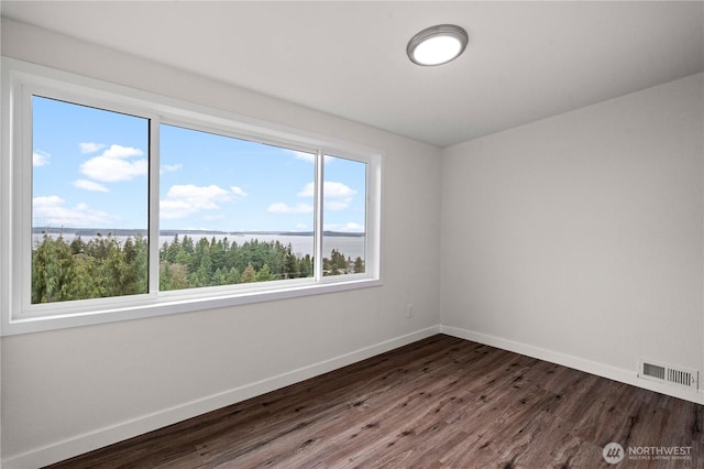 empty room featuring dark wood-style floors, visible vents, baseboards, and a water view