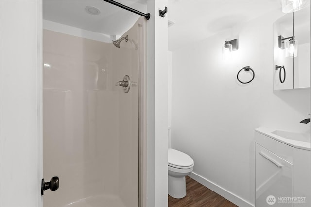 bathroom with toilet, a stall shower, wood finished floors, baseboards, and vanity